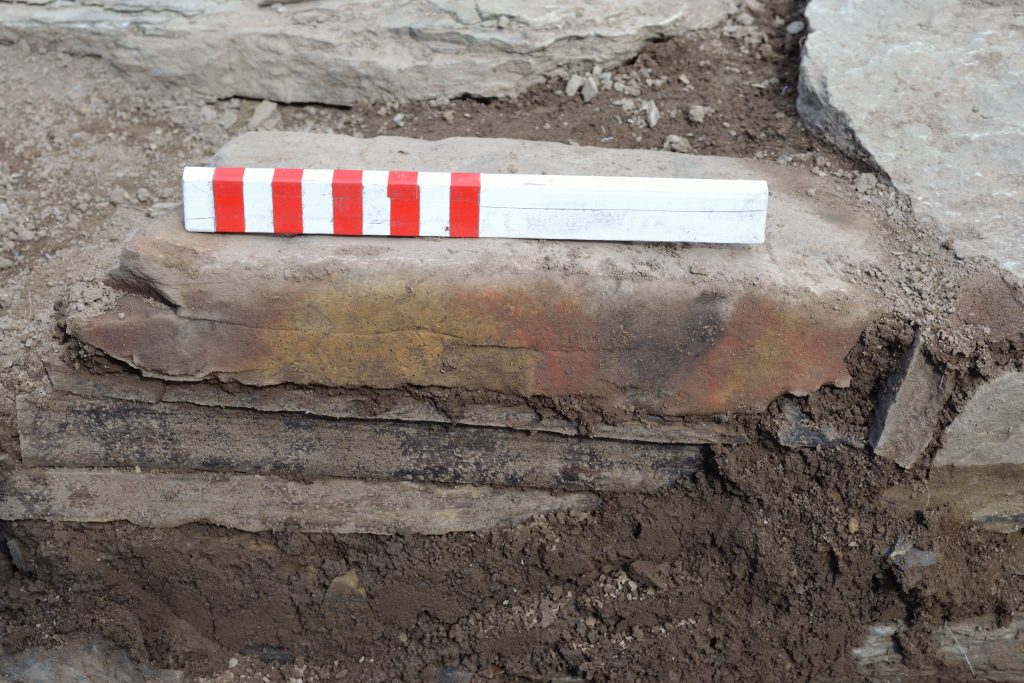Photograph of a painted piece of stone being uncovered in an archaeological trench