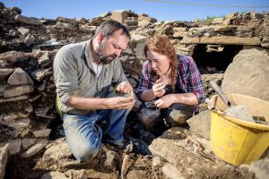 Photo of two people kneeling in a trench looking at an artefact