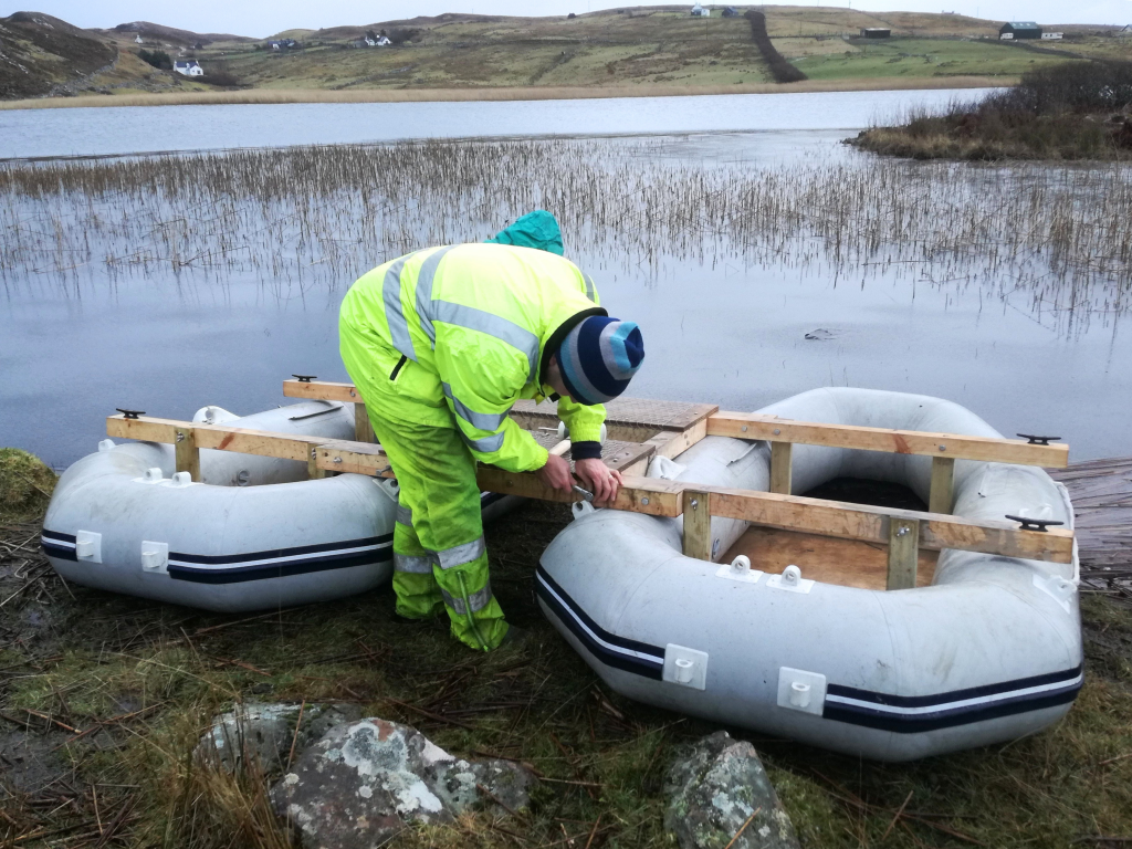 A person assembling core-collecting apparatus at Loch na Claise. The crannog can be seen in the background to the right.