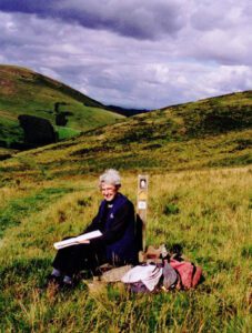 Photo of a woman sat drawing in a wild landscape