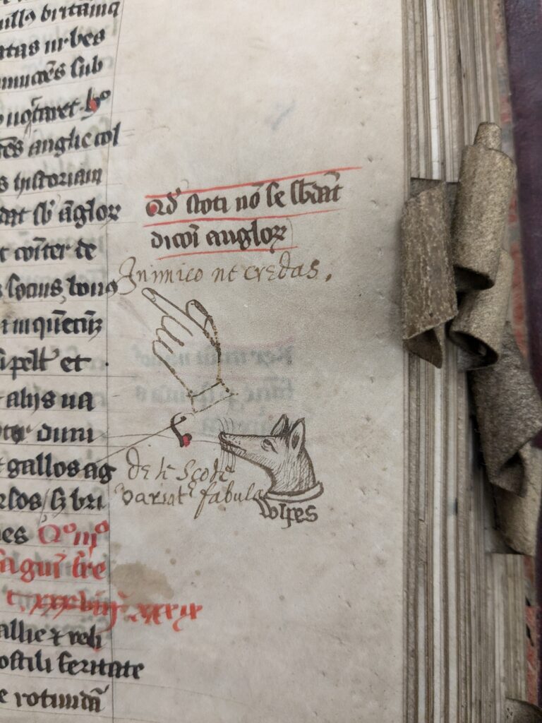 Photo of a pointed hand and a fox head in the margins of a medieval manuscript