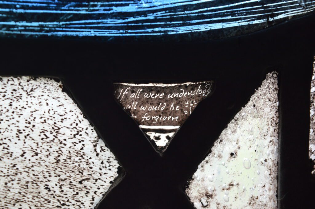 Miniscule inscription on stained glass, almost imperceptible to the eye, reading “If all were understood, all would be forgiven”.
