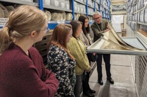 Photo of five people gathered around a drawer in an archive store and looking at a pile of maps
