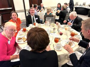 Photo of a group of people sat around a round table in a conference room enjoying dinner