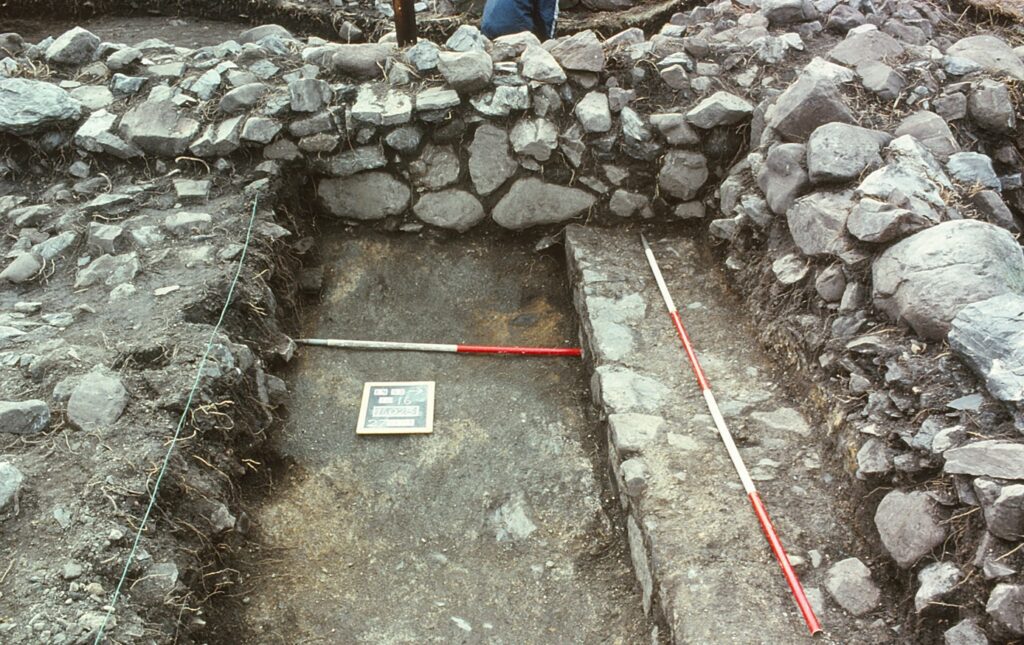 A 1m ranging rod on the mortar floor of the castle and a 2m rod on the reduced remains of the interior eastwest castle wall in a trench 