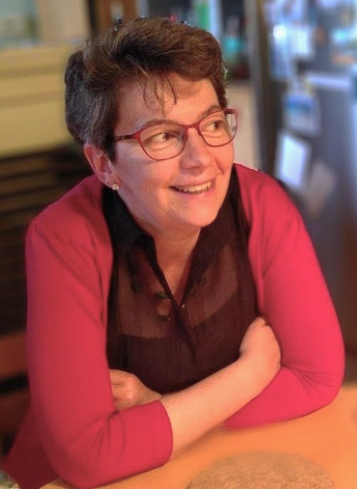 Photo of a woman with short dark hair, red-rimmed glasses wearing a red cardigan and smiling