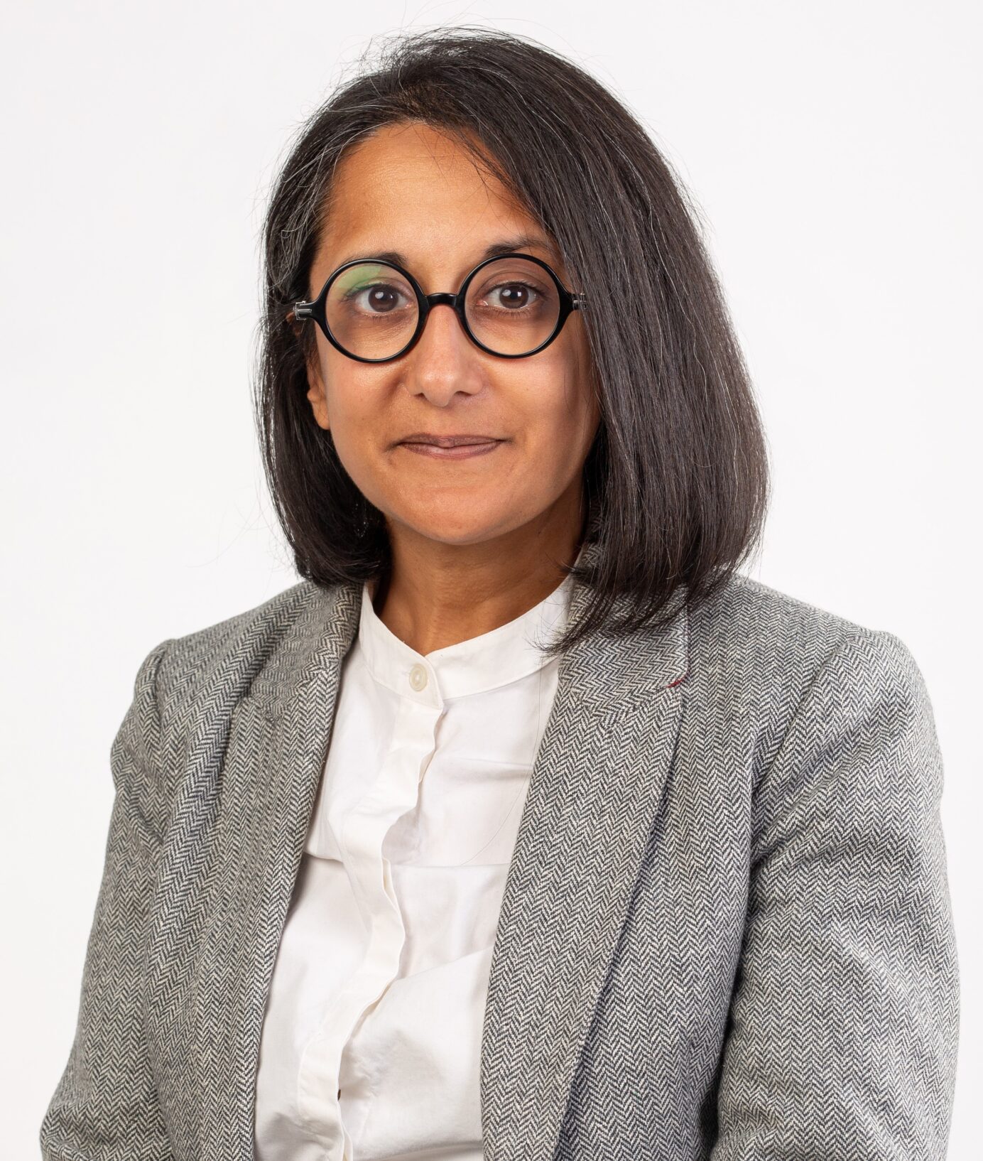 Photo of a woman in round black-rimmed reading glasses with straight dark shoulder-length hair wearing a white shirt and grey blazer