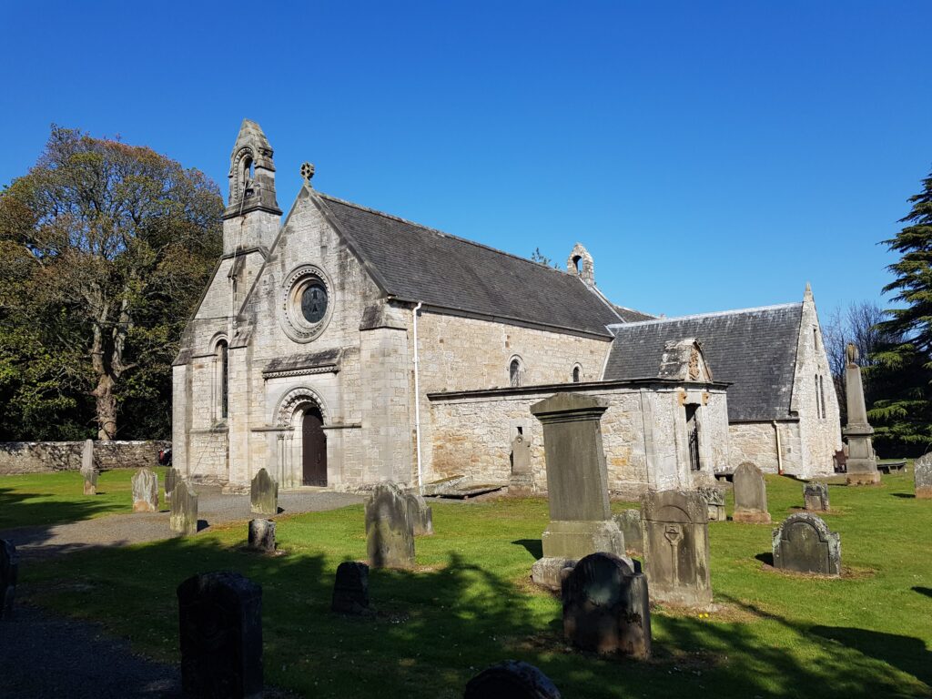 Photo of a small stone parish church and graveyard under a blue sky
