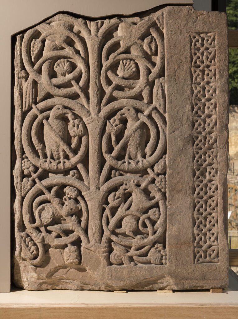 A close-up image of a stone panel carved with vines and small woodland animals eating grapes