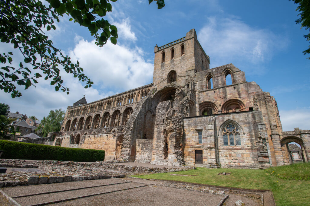 : Photo of the exterior of a medieval abbey with a tower, a roofless nave and exterior buildings visible