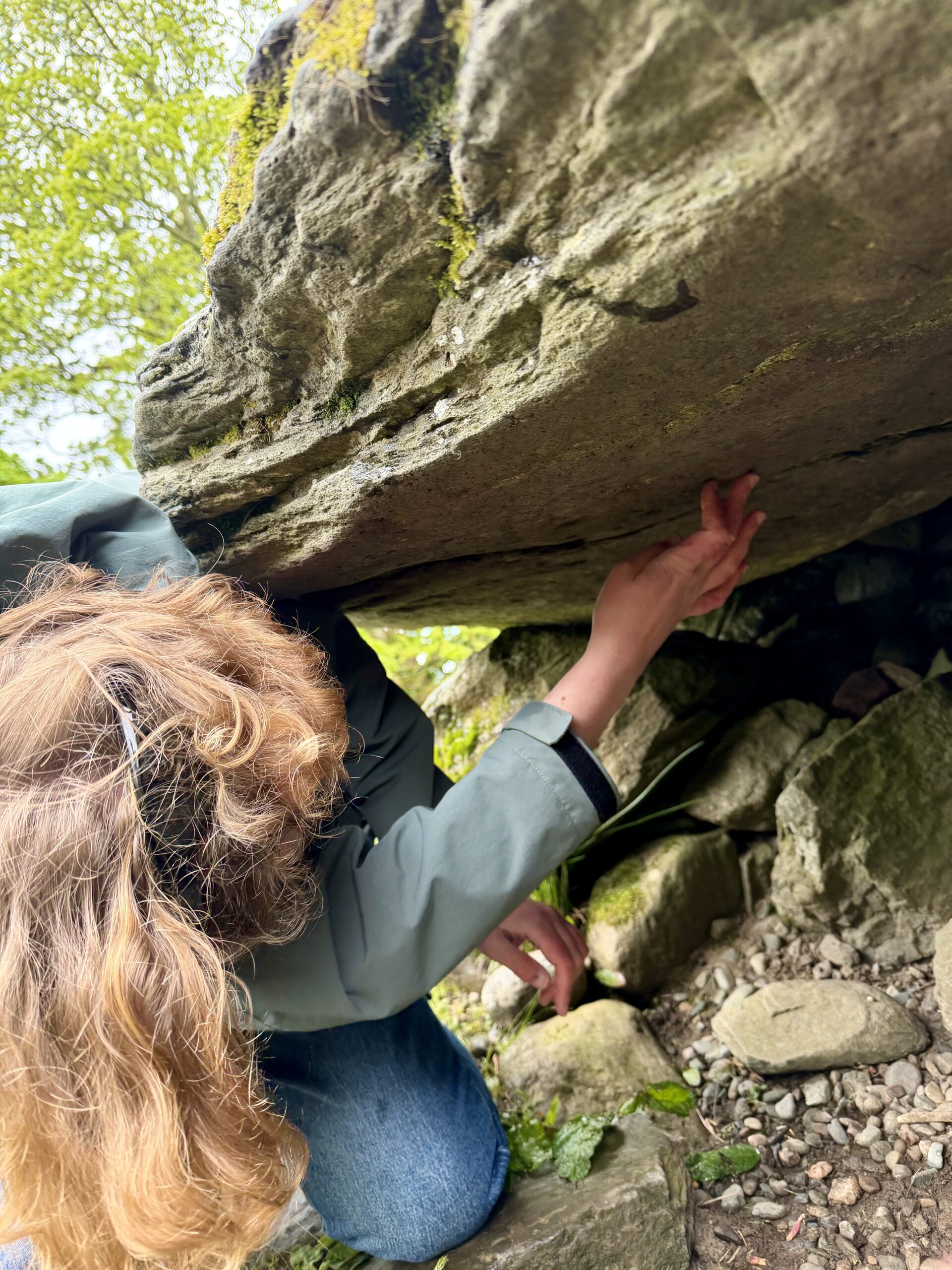 A participant at the Kilmartin Rock Art symposium investigating the deer carvings at Dunchraigaig cairn © ScARF Someone in outdoor clothing leaning by and looking at a rocky outcrop